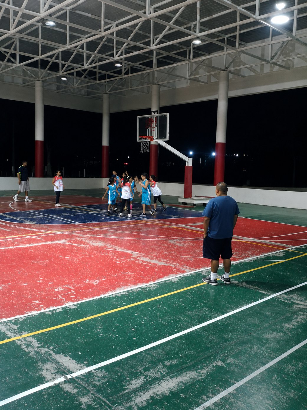 Iván Contreras Cárdenas observando entrenar a jóvenes jugadoras de basketball en el polideportivo de Colima por la noche